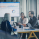 Finance Team Meets In A Glass Conference Room To Review Dashboards